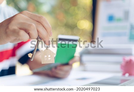 Man holding keys house with house shaped keychain and saving account passbook on wooden table.Real estate concept for buying a new home.
