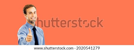 Portrait of smiling confident businessman showing thumbs up like hand sign gesture, over bright vivid orange background. Happy confident man gesturing. Mock up copy space ad area. Success in business.