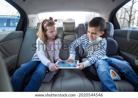 Brother and sister fighting over digital tablet on the back seat of the car, kids concept Royalty-Free Stock Photo #2020544546