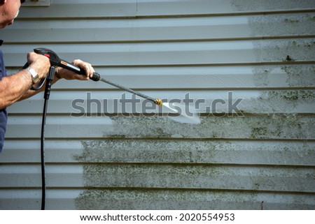 An unidentified man uses a power washer to clean mold and grime off the siding of a house. Royalty-Free Stock Photo #2020554953