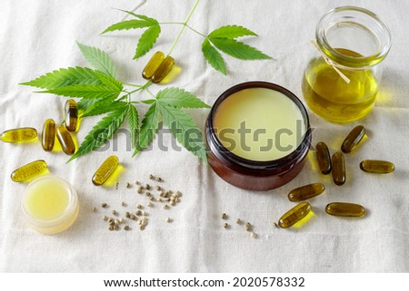 Cannabis medical healing salve, CBD capsules from sativa seeds, hemp oil bottle. Composition with cannabis leaves on fabric of hemp plants. Concept for treatment and relaxation or food supplements Royalty-Free Stock Photo #2020578332
