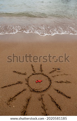 figure of a red plane and painted the sun on the sand on the coast. rest and tourism by plane to the sea. A picture of the sun and the symbol of the plane by the sea