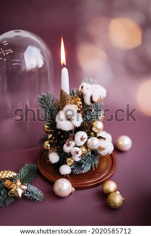 Beautiful festive floral winter composition of faux spruce, cotton, glitter, baubles, candle, stars, white berries inside a glass cloche on the burgundy coloured background, vertical photo
