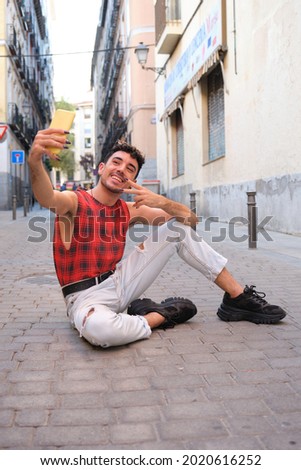Young caucasian man with long false nails taking a selfie with the smartphone sitting on the floor.