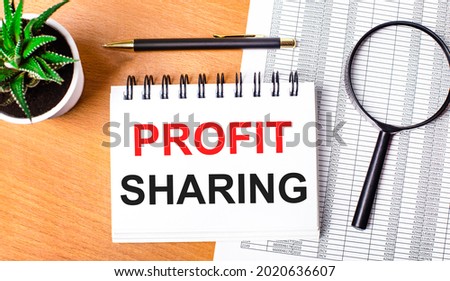 On a wooden table there are reports, a potted plant, a magnifying glass, a black pen and a notebook with the text PROFIT SHARING. Business concept