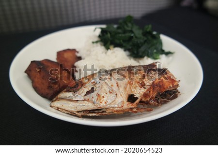 Fried fish served with rice, fried tofu and green vegetables as closeup view in white plate and isolated background. Asian food.