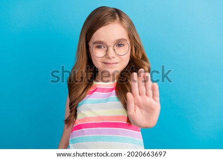 Photo of confident small girl raise hand show stop gesture wear specs striped dress isolated blue color background