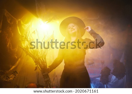 Young woman looking like witch having fun on Halloween in dark room with yellow light and smoke. Carnival concept and Halloween party