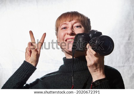 Female photographer in studio in black dress with camera on white background. Woman posing indoors with cam