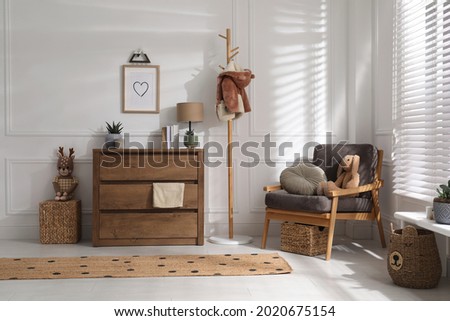 Stylish room interior with wooden chest of drawers and comfortable armchair