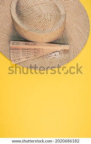 A round straw hat and a folding hand fan isolated on a yellow background with free space for text- concept for hot summer weather