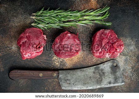 Fresh raw fillet minion steaks marbled beef with rosemary and garlic set, and old butcher cleaver knife, on old dark rustic background, top view flat lay