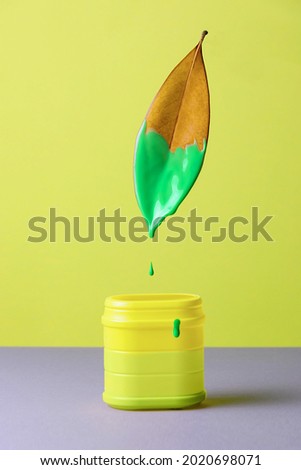 A dry magnolia leaf half painted with green paint levitate over a plastic can with dripping liquid. Creative concept of unfair marketing, greeenwashing, the end of summer. Royalty-Free Stock Photo #2020698071