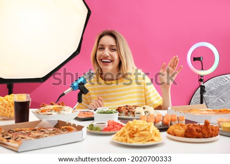 Food blogger recording eating show near microphone at table against pink background. Mukbang vlog
