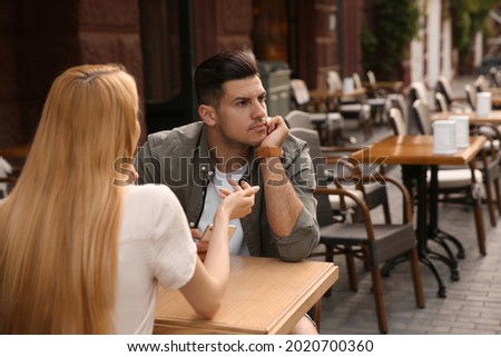 Man getting bored during first date with overtalkative young woman at outdoor cafe Royalty-Free Stock Photo #2020700360