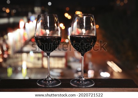 Glasses of red wine on wooden surface against blurred cityscape. Modern outdoor terrace