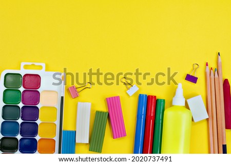 watercolor paints, colored plasticine, paper clips, felt-tip pens, glue, pencils on yellow background