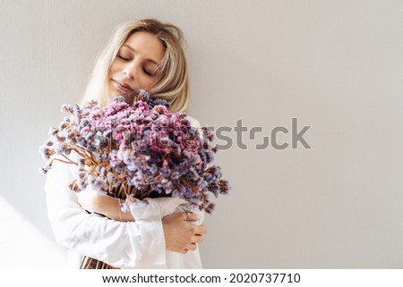 Portrait of young girl in white shirt, holding a big bouquet of dried flowers over gray background splashed by lines of light