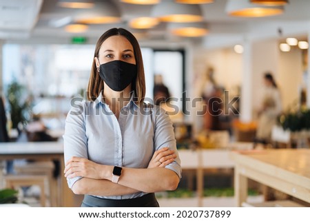 Woman business owner wearing face mask after reopening restaurant, arms folded