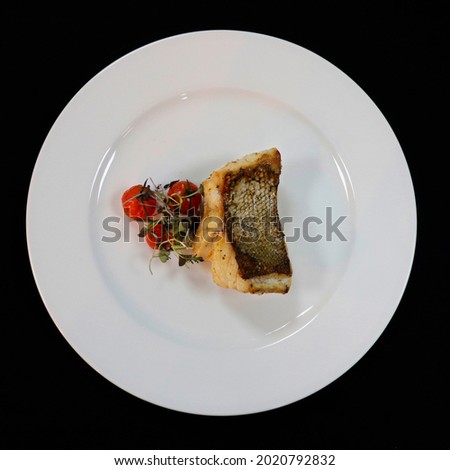 grilled white fish fillet on a white plate with cherry tomato