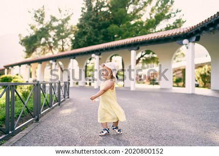 Little girl is spinning on the gravel path near the gazebo in the park