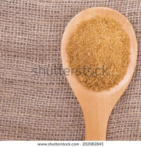 Brown sugar in wooden spoon on gunny sack background