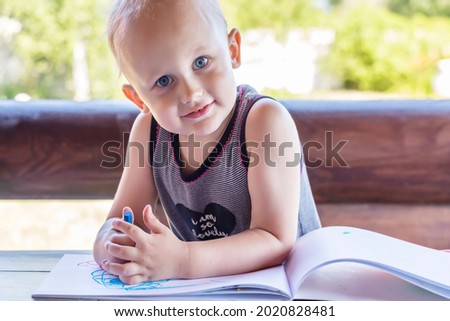 The kid drawing with wax crayons, smiling looks at the camera