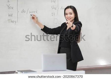 Stock photo portrait of a confident cheerful Asian woman teacher in a black business suit uniform with a digital tablet and laptop to teach modern language in the classroom