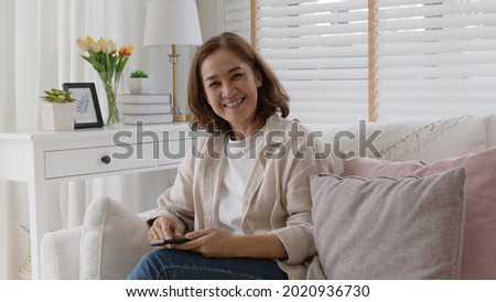 Old adult asia curly hair female sitting easy relax on sofa couch toothy smile looking at camera at cozy home for happy early retired in older people, elderly mental health care, aging skin lady face. Royalty-Free Stock Photo #2020936730