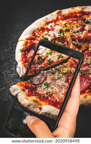 woman hand holding and showing smart phone takes a photo Pizza with Mozzarella cheese, ham, tomato sauce, salami, onion, pepper. food photos
