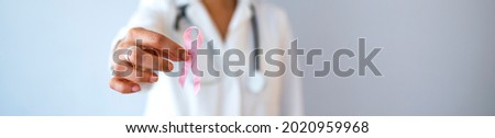 Doctor Hands Holding Pink Cancer Awareness Ribbon. Doctor with pink ribbon on color background, closeup. Breast cancer awareness concept. Cancer awareness concept