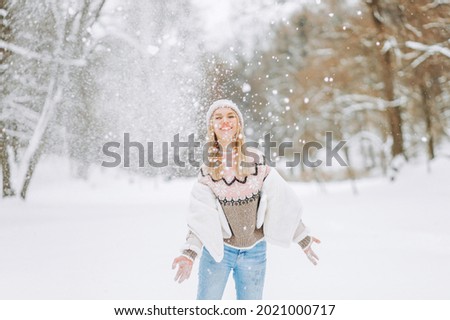 Happy blond woman plays with a snow in winter day. Girl enjoys winter, frosty day. Playing with snow on winter holidays, a woman throws white, loose snow into the air. Walk in winter forest.