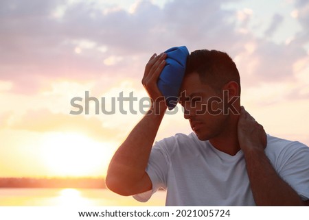 Man with cold pack suffering from heat stroke near river at sunset Royalty-Free Stock Photo #2021005724