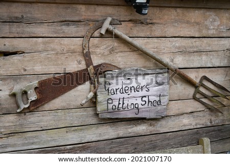 Gardeners Potting Shed sign, with fork and saw hanging on wooden shed
