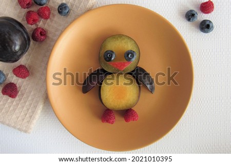 A funny baby bird made of fruit on a ceramic plate. Blueberries, plums, grapes and apples were used for production. A creative idea for decorating food.