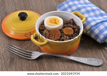 Lentil casserole dish with carrot slices and a slice of hard-boiled egg next to a fork and a checkered napkin close-up on wooden background 
