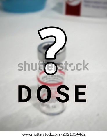 Wording DOSE and question mark symbol. Empty vaccine bottle background. Concept how many Covid-19 vaccine doses needed. White and out of focus background. Malaysia
