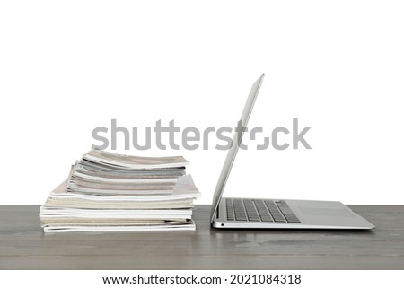 Stack of magazines and laptop on table near white wall
