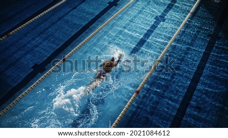 Female Swimmer Racing in Swimming Pool. Professional Athlete Overcoming Stress and Hardships in Dark Dramatic Pool, Cinematic Lap Lane Light Showing the Good Way. Aerial Shot Royalty-Free Stock Photo #2021084612