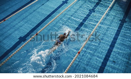 Beautiful Female Swimmer Using Front Crawl, Freestyle in Swimming Pool. Professional Athlete Training to Win Championship. Stylish Colors, High Angle Shot with Drammatic Light.
