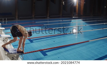 Muscular Male Swimmer Diving in Swimming Pool. Professional Athlete Standing on a Starting Block, Ready to Jump into Water. Training Determined to Win Championship. Shot with Stylish Colors Royalty-Free Stock Photo #2021084774