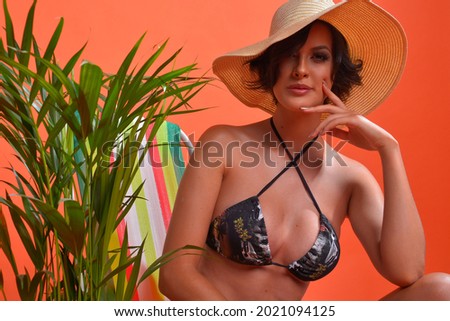 orange background, photo shoot in studio, bikini and beach hat.