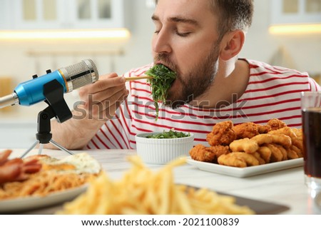 Food blogger eating near microphone at table in kitchen, closeup. Mukbang vlog