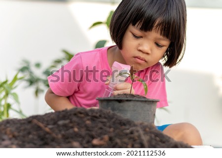 Cute Asian Thai kid girl wearing a pink shirt using Pocky watering the seedlings Her tree had just been planted in a pot, beside it was a pile of black soil. She was a child who loved nature.