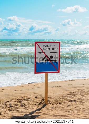 No swimming warning sign on the beach with waves in the background. Inscription in Russian "Swimming is prohibited"