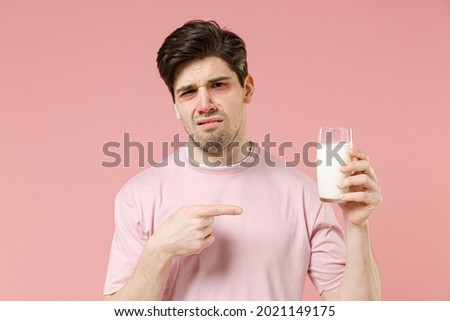 Sick sad unhealthy ill allergic man has red watery eyes, runny stuffy sore nose suffer from intolerance lactose allergy trigger symptoms hold milk glass isolated on pastel pink color background studio Royalty-Free Stock Photo #2021149175