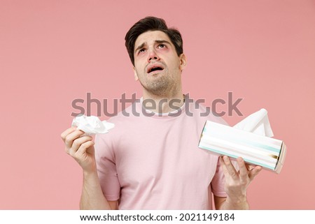 Sick unhealthy ill allergic man has red watery eyes runny stuffy sore nose suffer from allergy trigger symptoms hay fever hold paper napkin handkerchief isolated on pastel pink color background studio Royalty-Free Stock Photo #2021149184