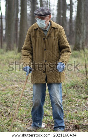 Pensioner in an old jacket. Russian old man in a medical mask on the street. An old person with a disability. An old man in Russia. A man with a walking stick.