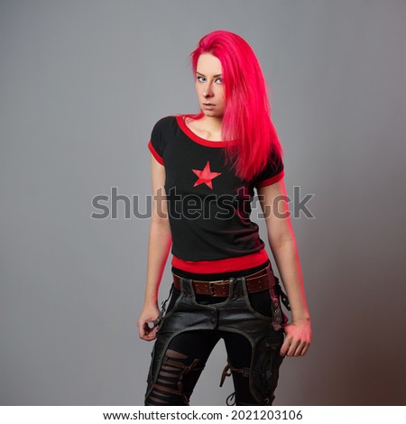 Kitsch style, fashion of the future. mixing styles. A young woman with bright scarlet hair in dark unusual clothes on a gray background