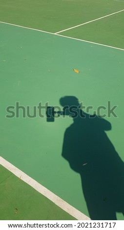 shadow photo of a boy on a green tennis court